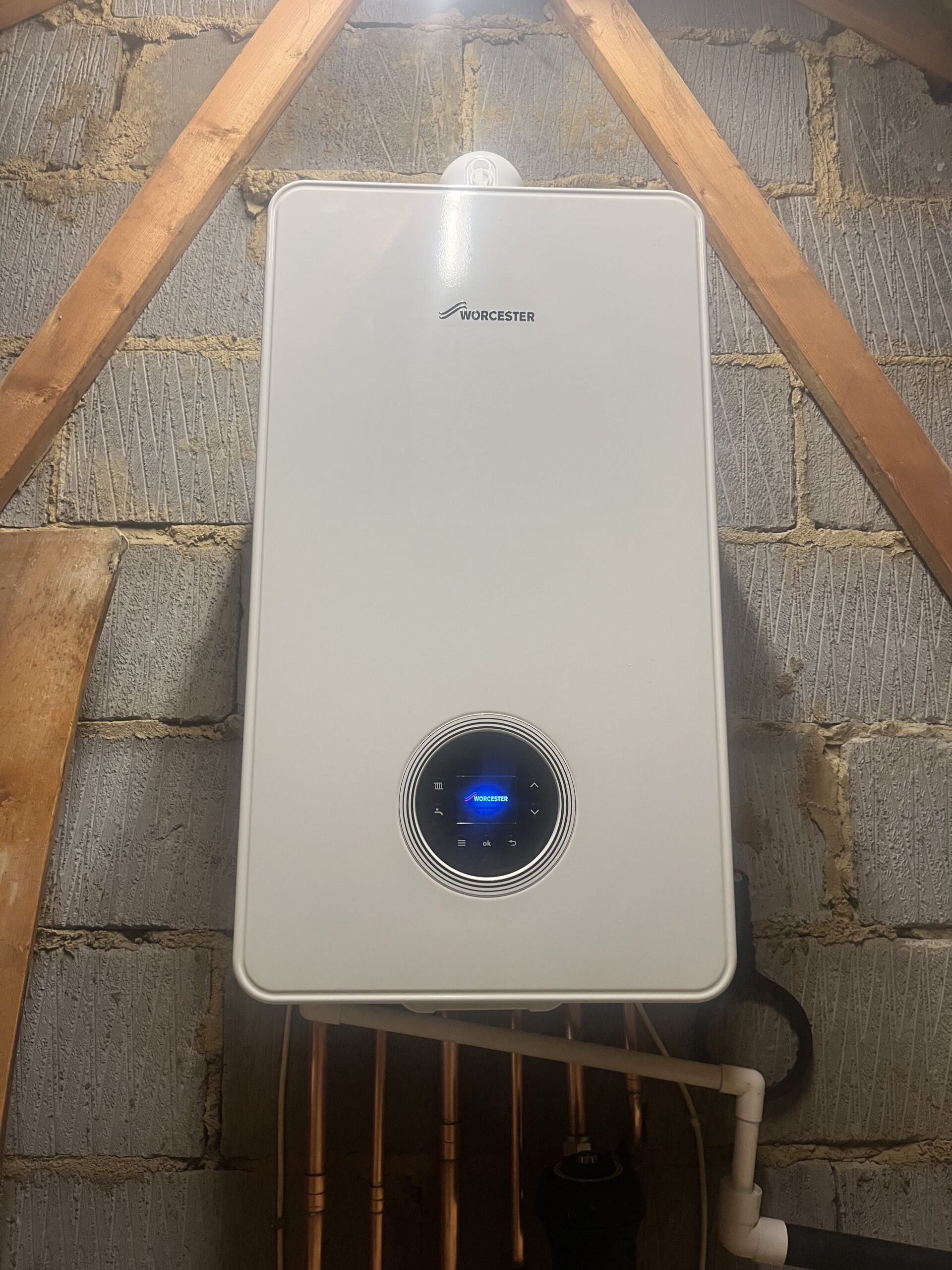 A new white boiler with a blue display, fitted on a wall above tidy pipework