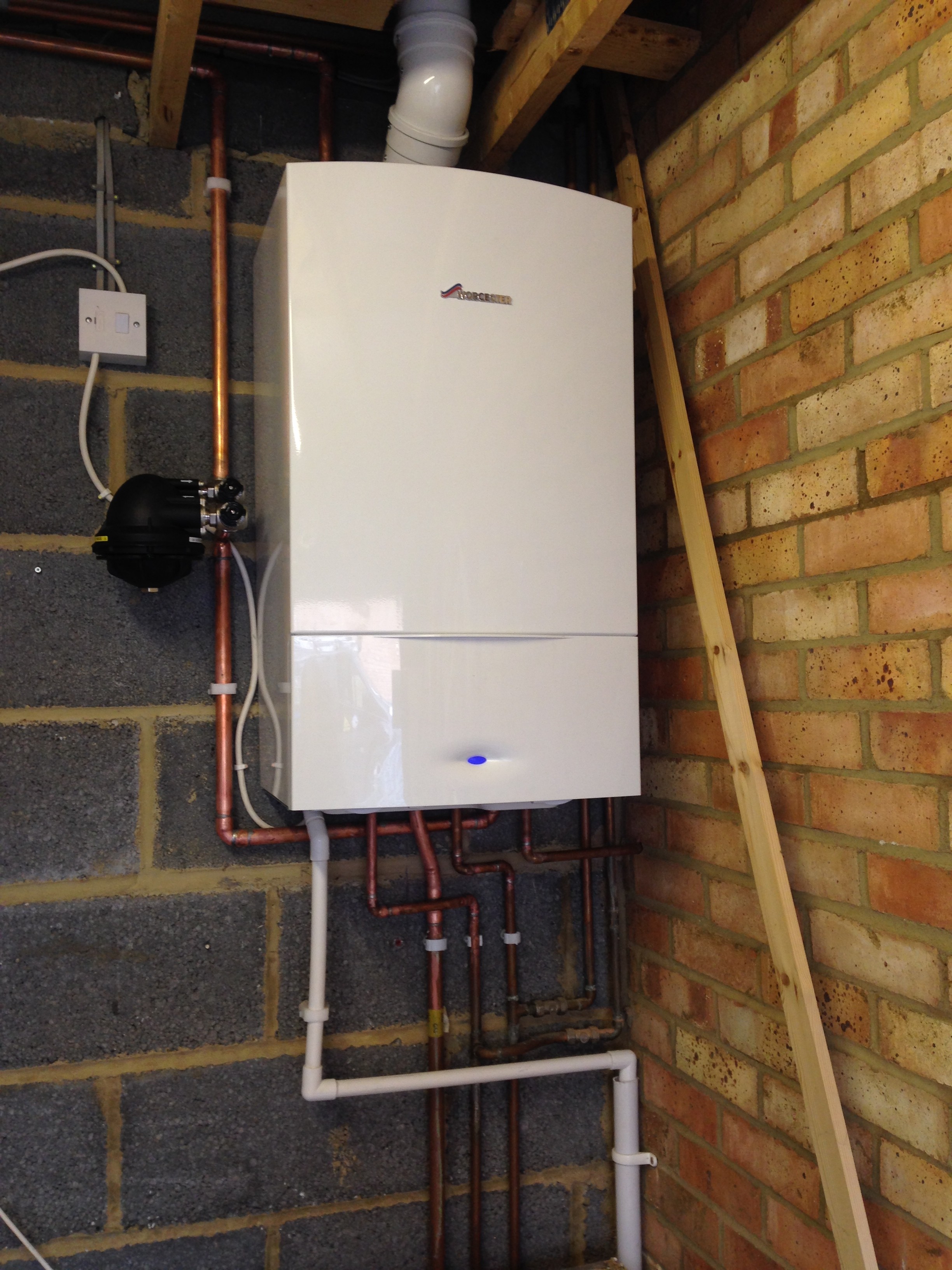 A white boiler installed in an outbuilding with new pipework